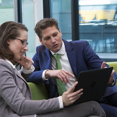 Camerabeelden op een tablet Een sfeerbeeld van een man in een blauw pak die wat aanwijst op een tablet aan de vrouw die links bij hem op een groene bank zit.